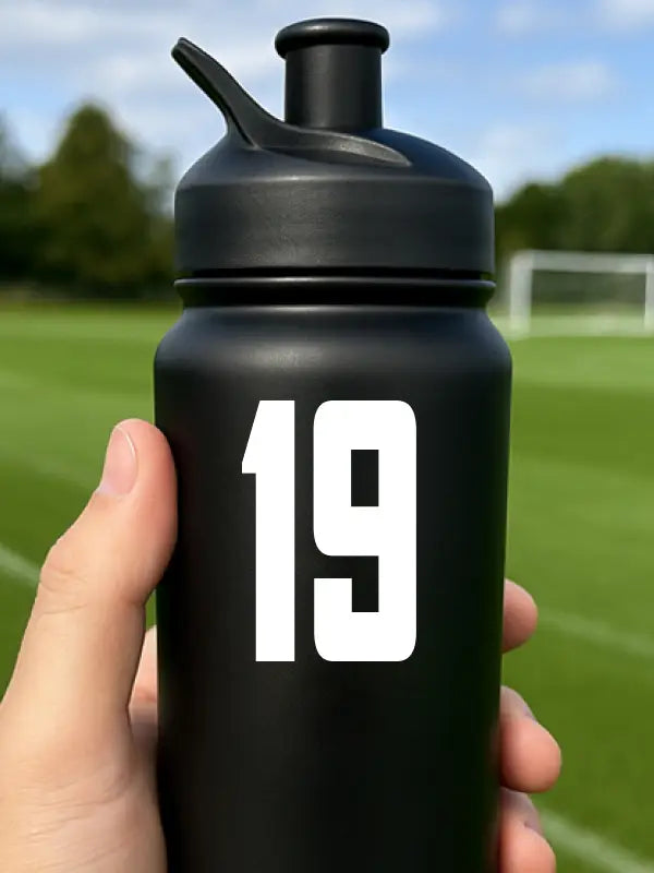 Black bottle on football pitch featuring bold white personalised bottle sticker number 19 for sports teams.