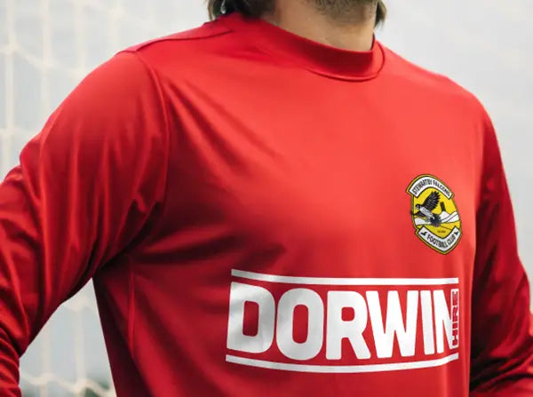 Football shirt with bold white iron-on transfer showing sponsor name and team badge on red fabric.