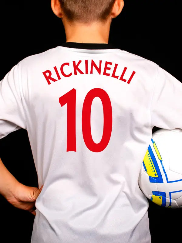 Youth wearing white football shirt with 'RICKINELLI' and number 10 in bold red football name and number iron on transfers.