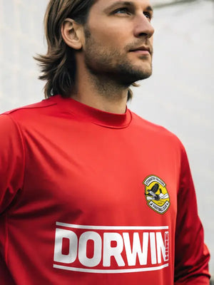 Footballer wearing red top featuring large iron on sponsor transfer on chest