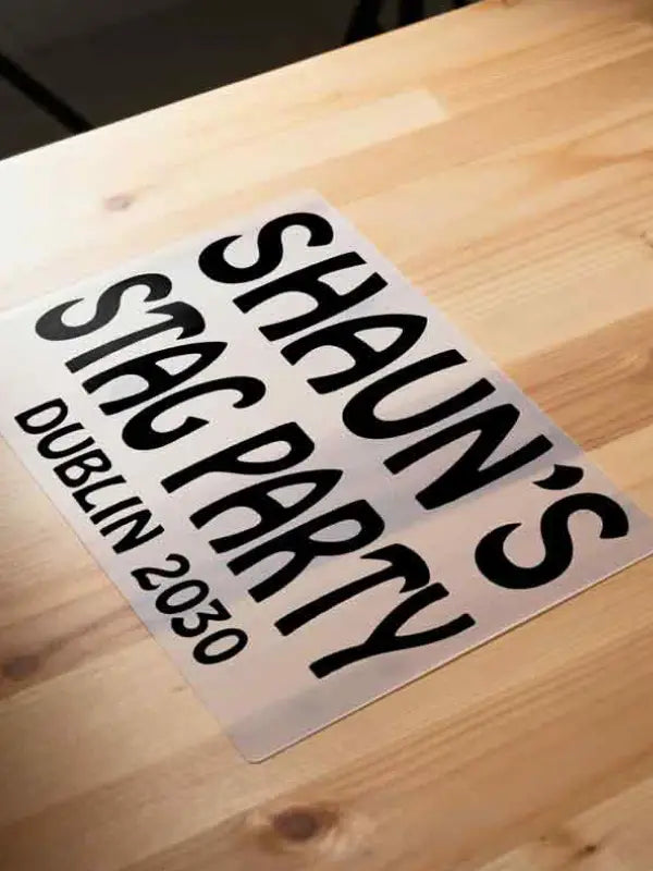 Iron on stag party transfer on clear carrier film placed on a wooden surface, displaying black text ready to be applied with a household iron.