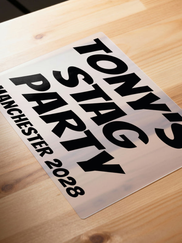 Iron on stag party transfer on clear carrier film placed on a wooden surface, displaying bold black text “Tony’s Stag Party Manchester 2028” ready to iron on.