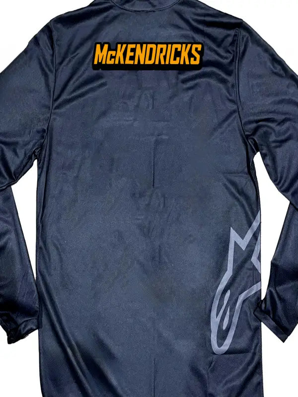 Close-up of a black motocross jersey showing the name only with McKendricks in bright orange iron on transfers with black shadows.