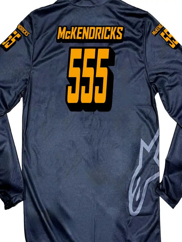Close-up of a black motocross jersey showing the name McKendricks in bright orange iron on transfers with black shadows.