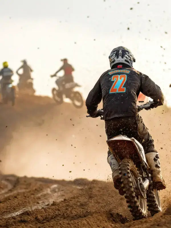 Motocross rider with race name and number iron on transfer on jersey, kicking up dirt during a race on rugged off-road terrain